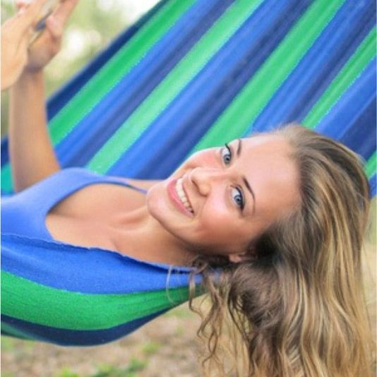 2 persoonshangmat - blauw/groen with a smiling woman relaxing in a durable blue and green cocoon hammock outdoors